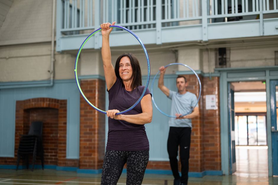 Hai người cao tuổi mỉm cười và tập thể dục vui vẻ với hula hoop trong buổi tập nhóm tại trong nhà.