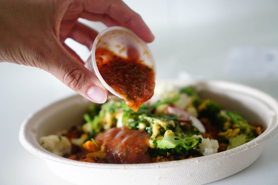 Hand pouring sauce over a colorful vegetable salad bowl, representing mindful time-conscious eating