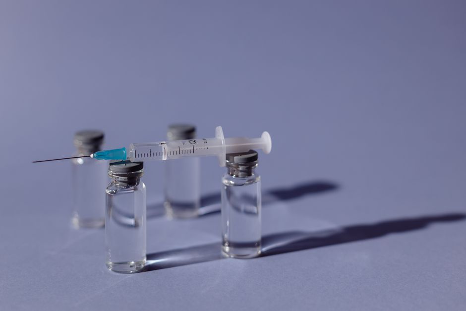 A syringe balanced on vaccine vials with a purple backdrop, representing medical treatment.